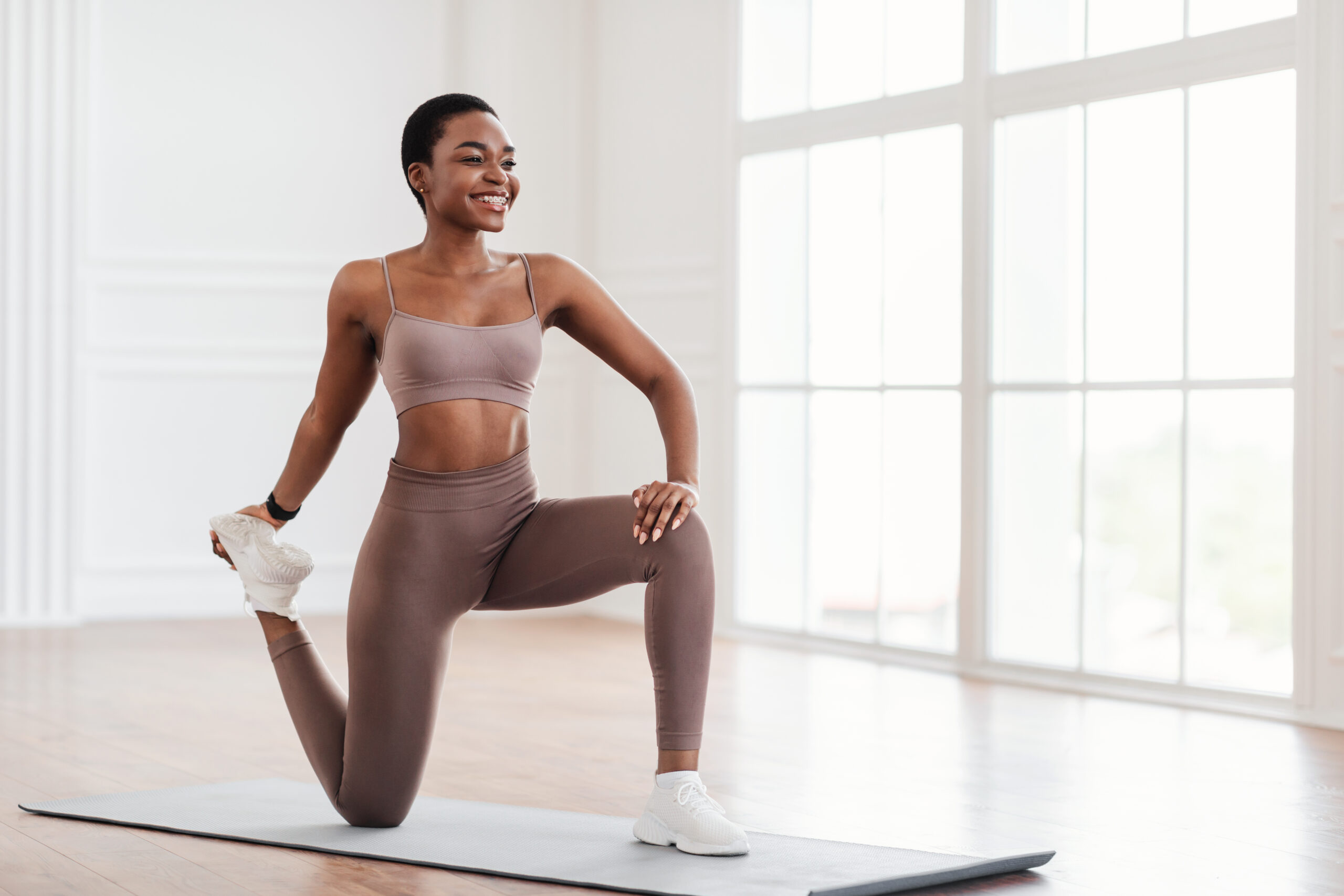 Happy young black woman stretching leg exercising on yoga mat - Recuro Health | Making Advanced Healthcare Accessible™
